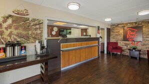 A reception area with a wooden reception desk, a Red Roof Inn sign, and a wall-mounted clock. - Red Roof Inn Atlanta South - Morrow (Morrow)