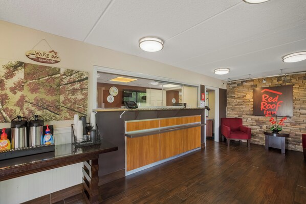 A reception area with a wooden counter, a clock, and a Red Roof Inn sign. - Red Roof Inn Atlanta South - Morrow (Morrow)