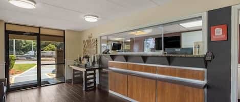 A hotel reception area with a wooden reception desk, a glass door entrance, and a Red Roof Inn sign.