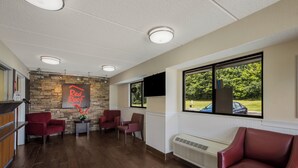 A reception area with a stone wall, red leather chairs, a reception desk, and large windows with a view of greenery. - Red Roof Inn Atlanta South - Morrow (Morrow)