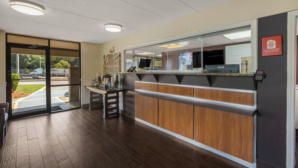 A reception area with a wooden counter, a glass door leading outside, and a ceiling with recessed lighting. - Red Roof Inn Atlanta South - Morrow (Morrow)