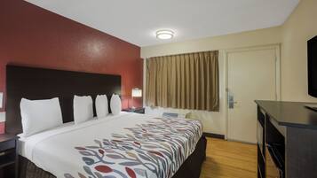 Una habitación de hotel con una cama, un escritorio, un televisor y una puerta.