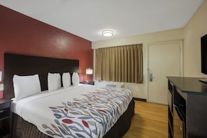 A hotel room with a bed, a desk, a television, and a door. - Red Roof Inn Atlanta South - Morrow (Morrow)