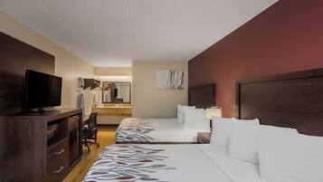A hotel room with a bed, a desk with a television, a mirror, and a bathroom visible in the background.