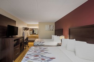 Habitación de hotel con una cama, un escritorio con televisor, un espejo y un baño visible al fondo.