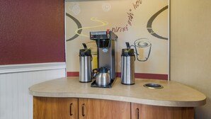 Una estación de café con una máquina de café, dos termos y una pared con una ilustración de una taza de café.
