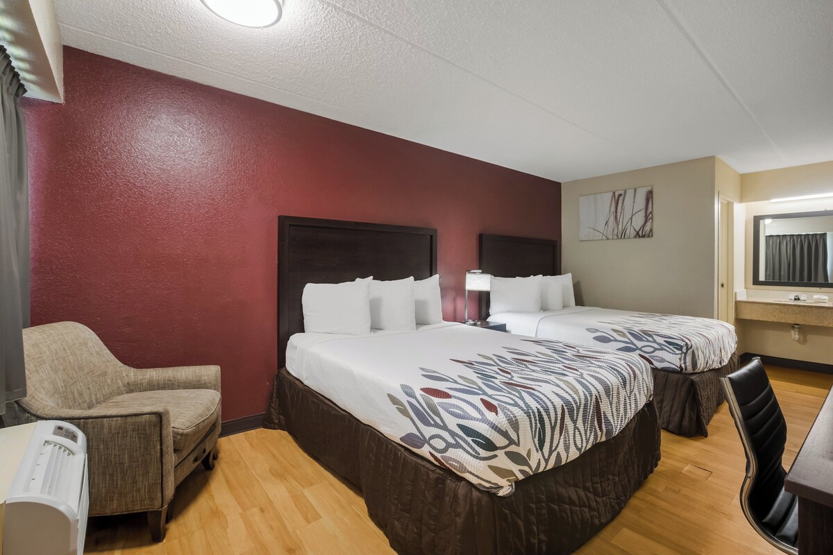 A hotel room with two beds, a chair, a desk, and a window.