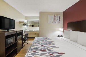 Una habitación de hotel con una cama, un escritorio con computadora, televisión y espejo.