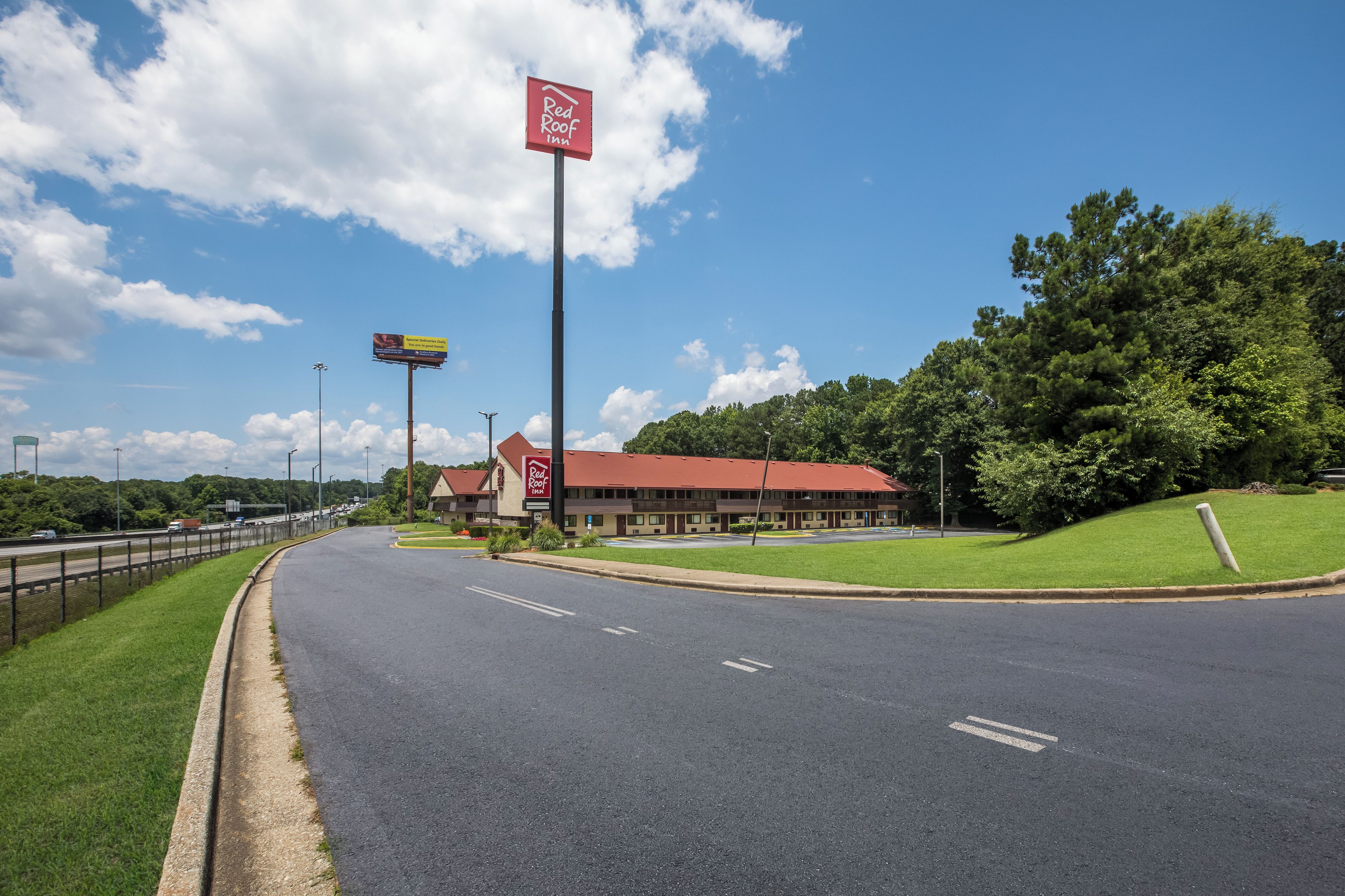 A Red Roof Inn with a red roof, located beside a highway with a clear sky.