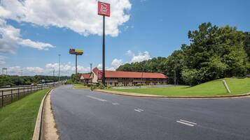 A Red Roof Inn with a red roof, located beside a highway with a clear sky.