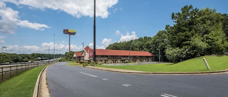 A Red Roof Inn with a red roof, located beside a highway with a clear sky.