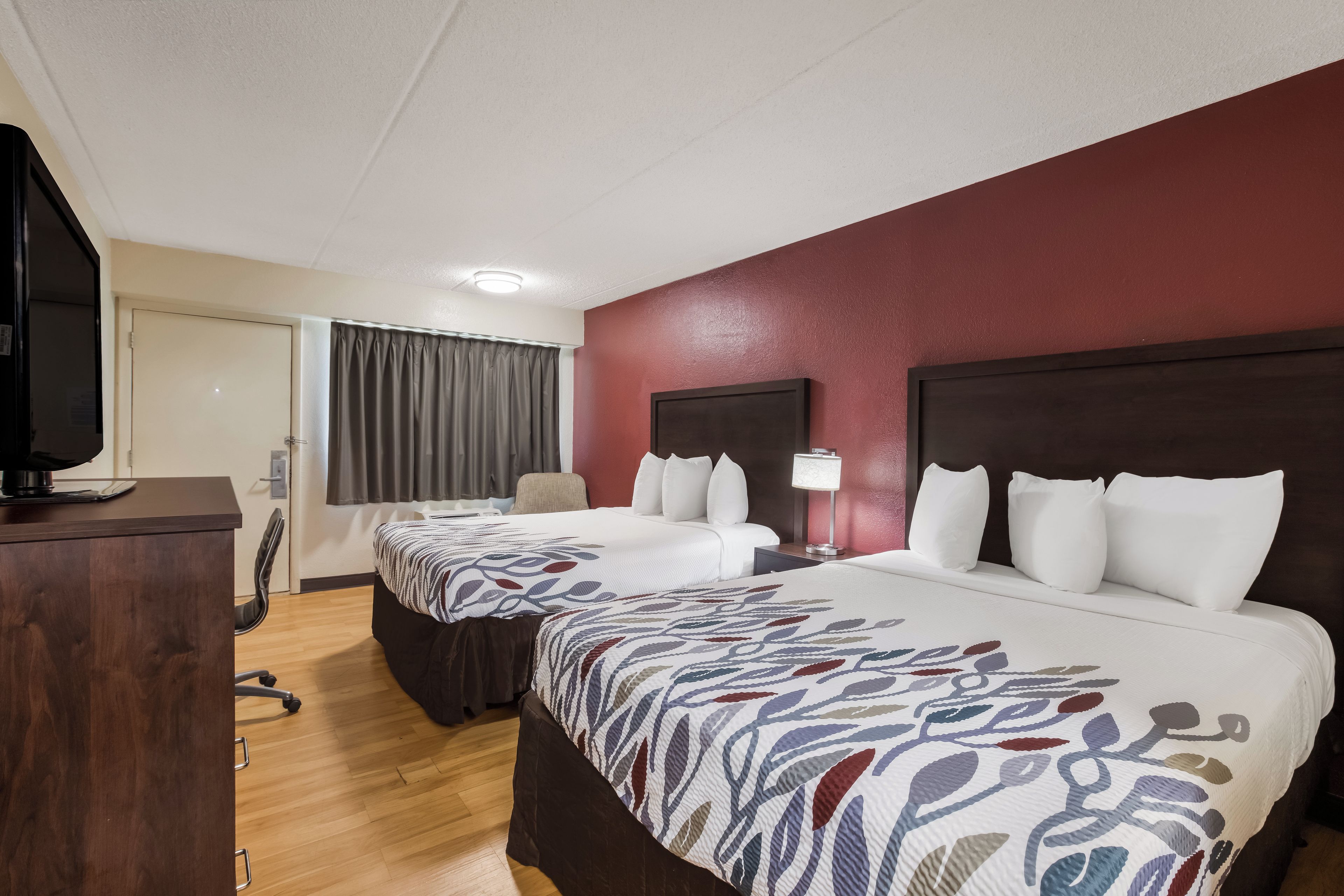 Une chambre d’hôtel avec deux lits, un bureau, une chaise et un téléviseur.