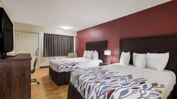 A hotel room with two beds, a desk, a chair, and a television.