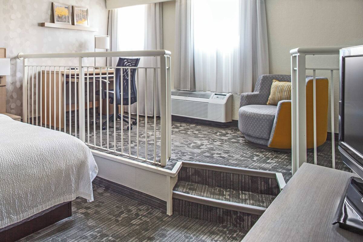 A hotel room with a crib, a sofa, a television, and a desk.