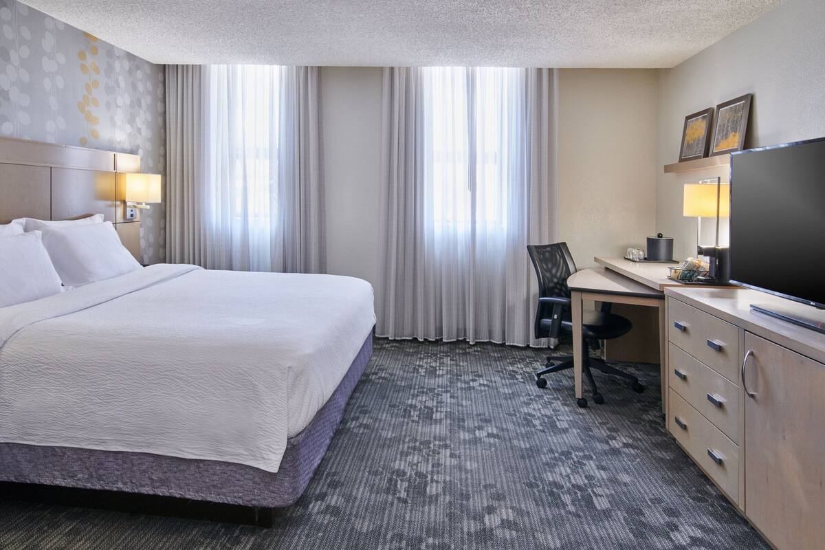A hotel room with a large bed, a desk with a chair, a television, and a window with curtains.