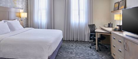 Una habitación de hotel con una cama grande, un escritorio con silla, televisión y ventana con cortinas.