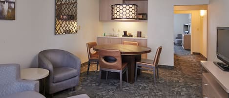 Une chambre d’hôtel comprenant un coin repas, un canapé, une télévision et un sol recouvert de moquette.