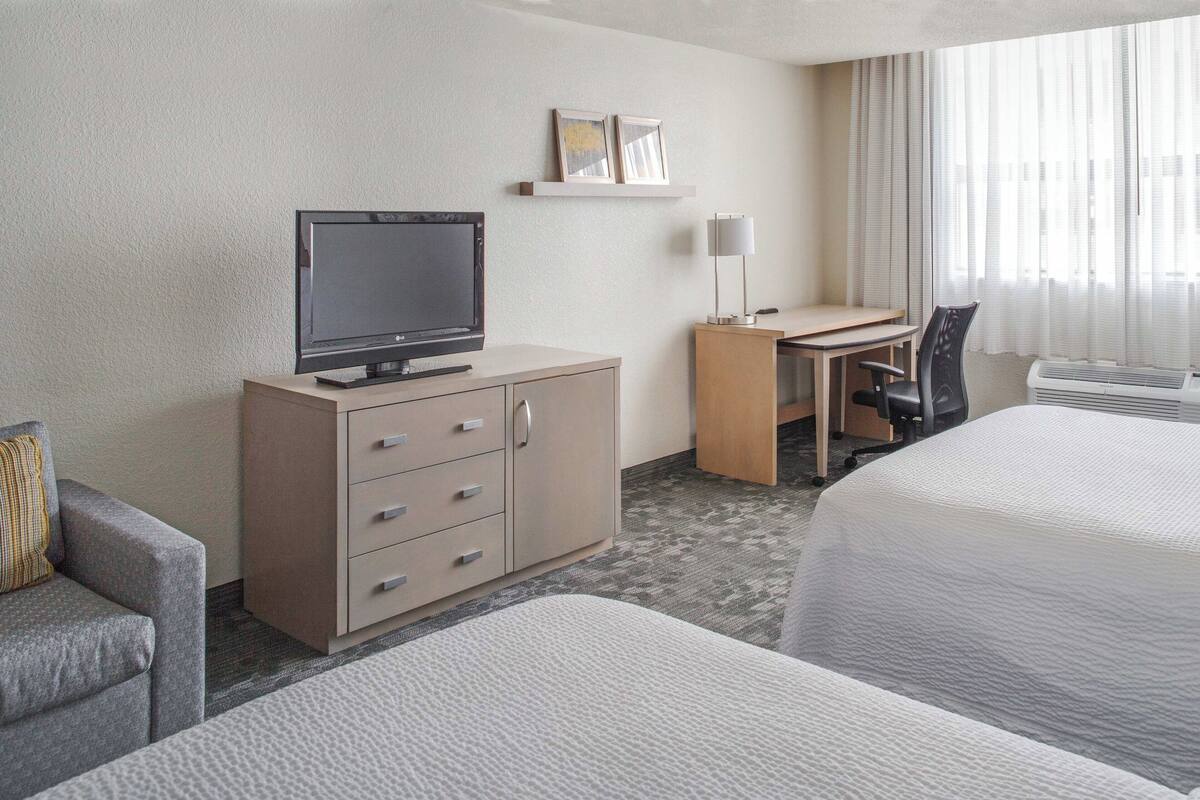 A hotel room with a bed, a desk with a chair, a television, a wardrobe, and a window with curtains.