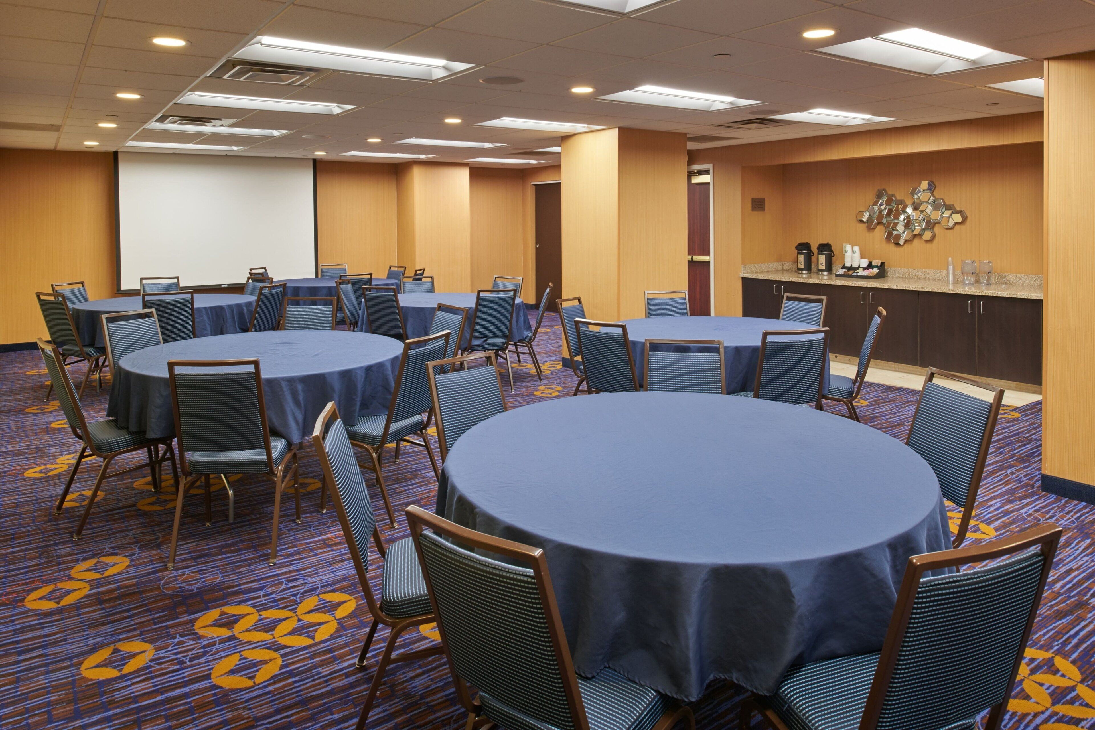 A conference room with round tables and chairs, a projector screen, and a coffee station.