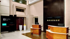 A modern reception area with a wooden reception desk, a 'Boarding Pass' sign, a large white planter, and a dark wooden wall. - Courtyard by Marriott Columbus Downtown (Columbus)