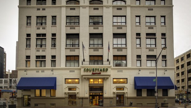 A multi-story hotel with a central entrance, large windows, and a blue awning. - Courtyard by Marriott Columbus Downtown (Columbus)