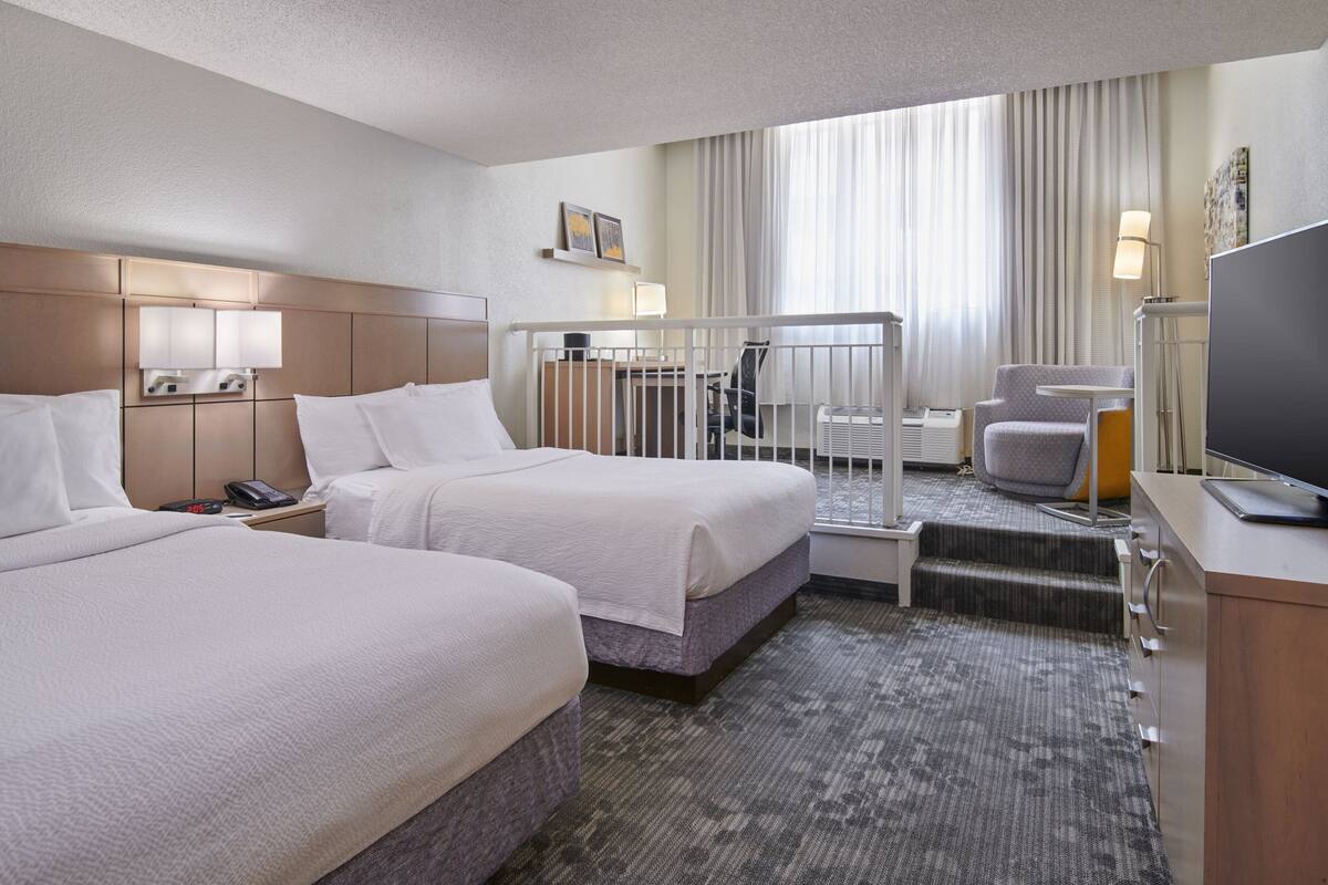 A hotel room with two beds, a desk with a computer, a TV, and a chair.