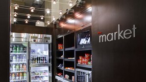 A refrigerated display area with shelves stocked with beverages and snacks, and a wall with the word "market" indicating a food service area. - Courtyard by Marriott Columbus Downtown (Columbus)