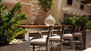 A modern dining area with a stone wall, a hanging plant, and a unique textured vase centerpiece. - Embassy Suites Hotel Baton Rouge (Baton Rouge)