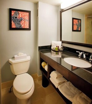 A modern bathroom with a toilet, sink, and large mirror. There are towels and toiletries on the counter.