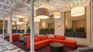 A modern lounge area with a large sectional sofa, a round coffee table, and a patterned carpet. - Embassy Suites Hotel Baton Rouge (Baton Rouge)