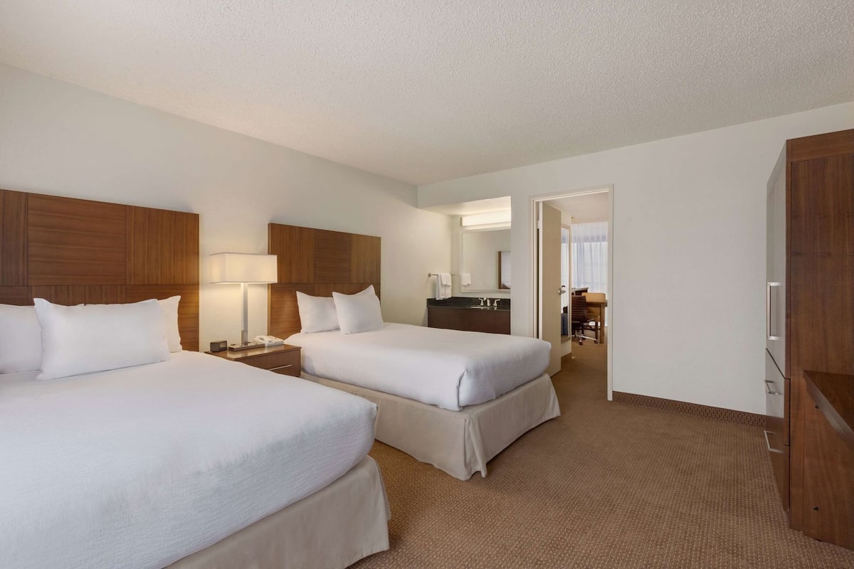 A hotel room with two beds, a bathroom, and a desk.