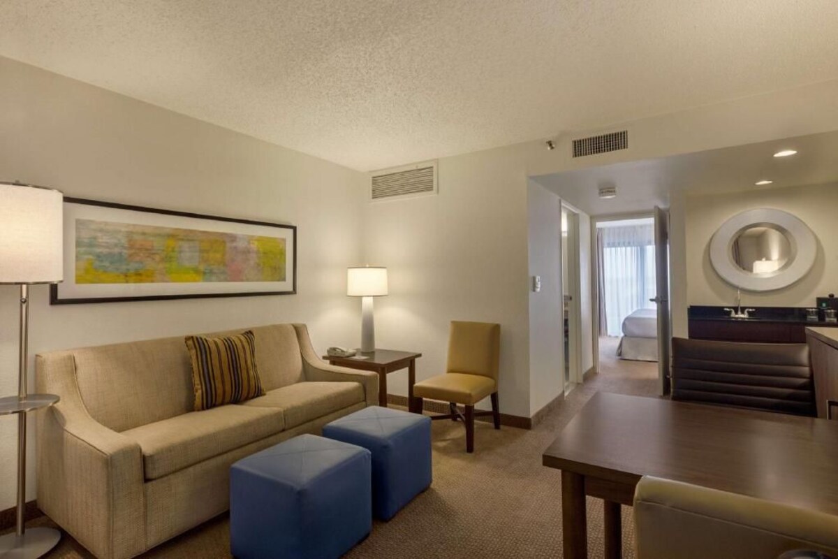 Une chambre d’hôtel comprenant un canapé, des poufs, une lampe, une chaise, une table à manger et un coin cuisine.