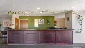 A reception desk with a green wall, a 'Quality' sign, and a 'by Choice Hotels' logo. - Quality Inn Los Lunas - Albuquerque South (Los Lunas)