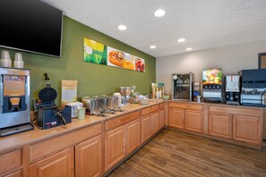 A kitchen area with a waffle maker, coffee machines, and a refrigerator.