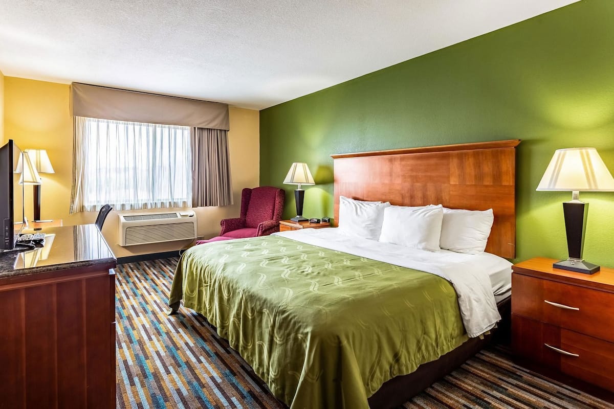 A hotel room with a bed, desk, chair, and a television.