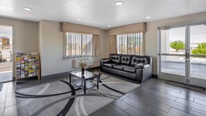 A modern lobby with a leather sofa, a glass coffee table, a magazine rack, and large windows. - Quality Inn Los Lunas - Albuquerque South (Los Lunas)