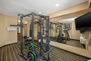 A gym with weightlifting equipment, a television, and a mirror.