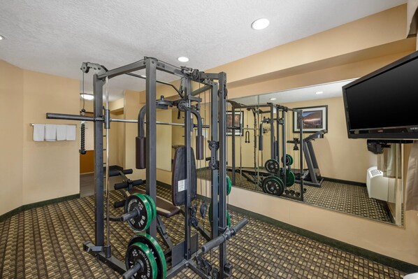 A gym with weightlifting equipment, a television, and a mirror.