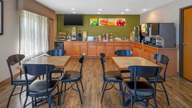 A dining area with a wooden table and chairs, a kitchen counter with coffee machines, and a TV mounted on the wall. - Quality Inn Los Lunas - Albuquerque South (Los Lunas)