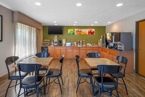 A dining area with a wooden table and chairs, a kitchen counter with coffee machines, and a TV mounted on the wall.