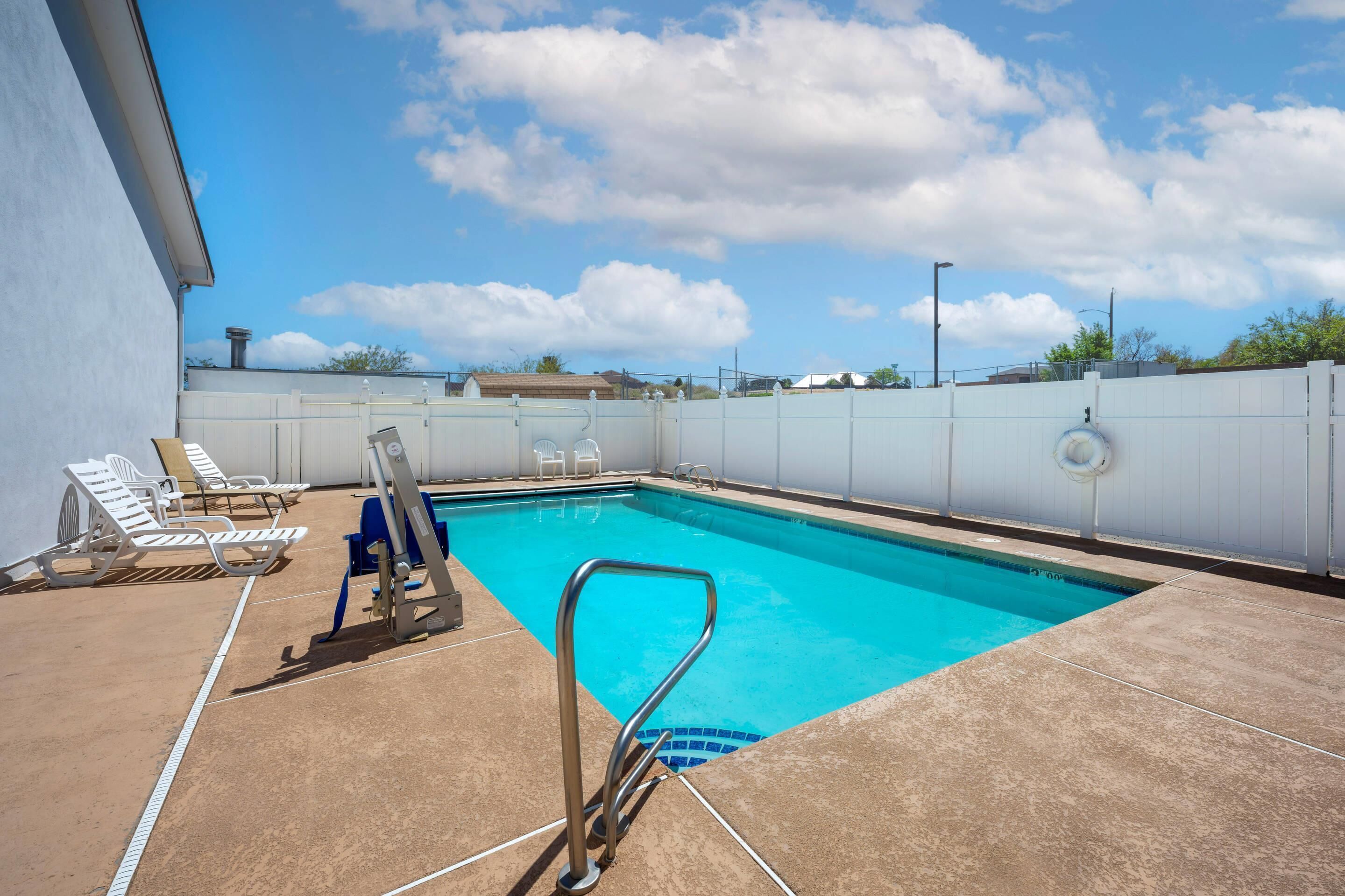 A swimming pool with a metal ladder, lounge chairs, and a white fence.