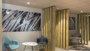 A modern waiting area with a wooden partition, two blue chairs, a small table, and a camera on the ceiling. - ibis Avignon Sud (Avignon)
