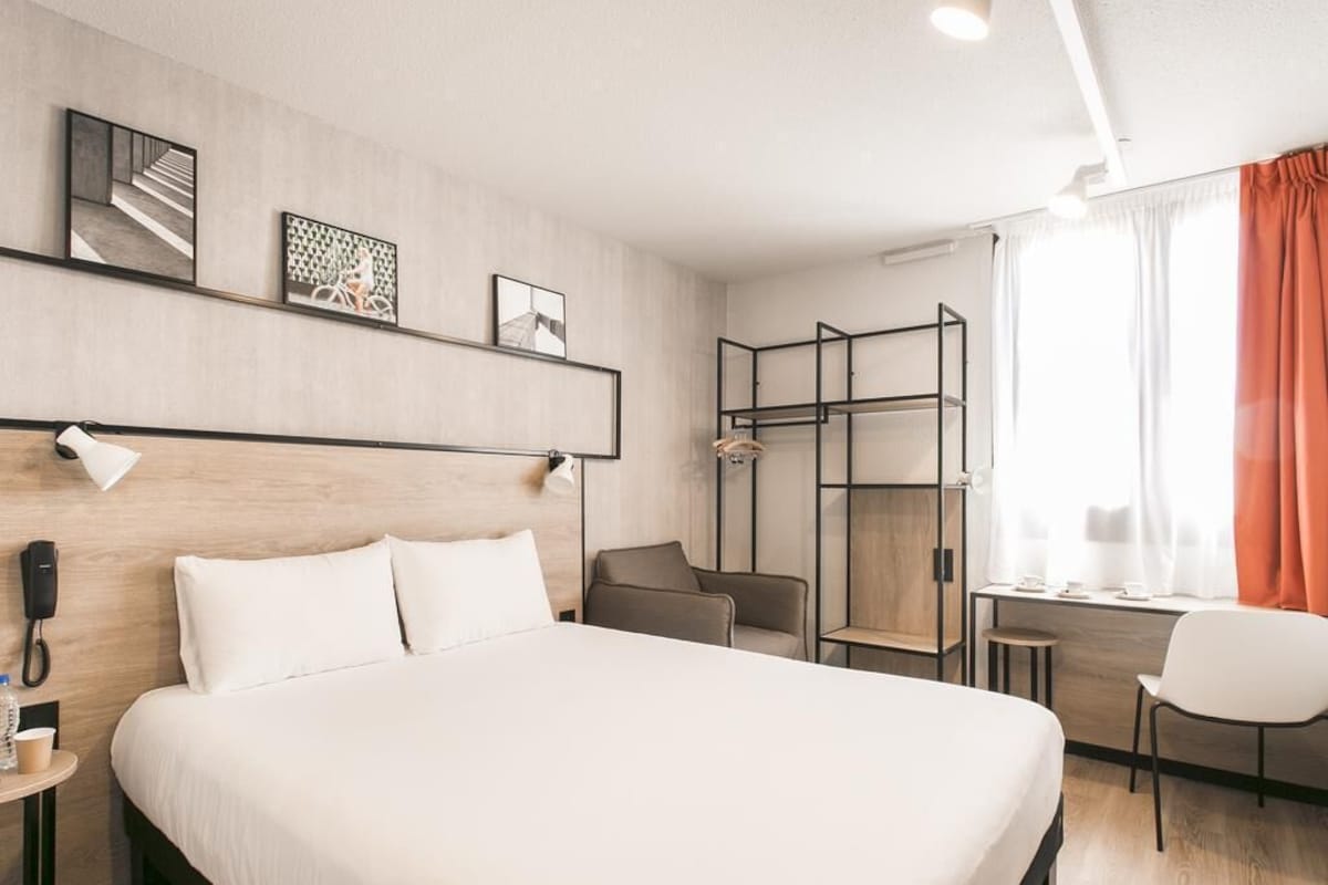 A hotel room with a large bed, a desk, a chair, a phone, and artwork on the wall.