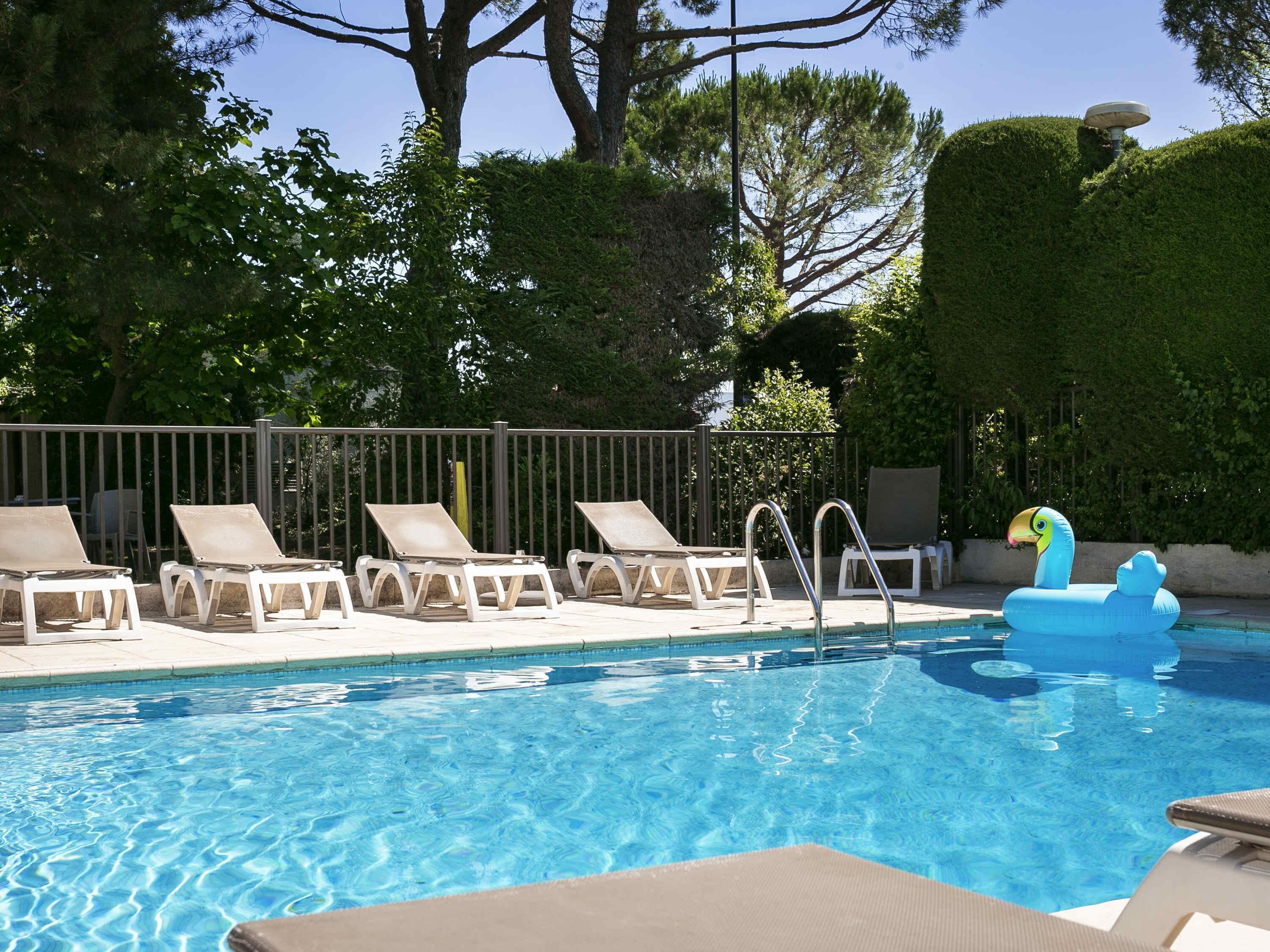 Una piscina al aire libre, sombrillas, sillones reclinables de piscina