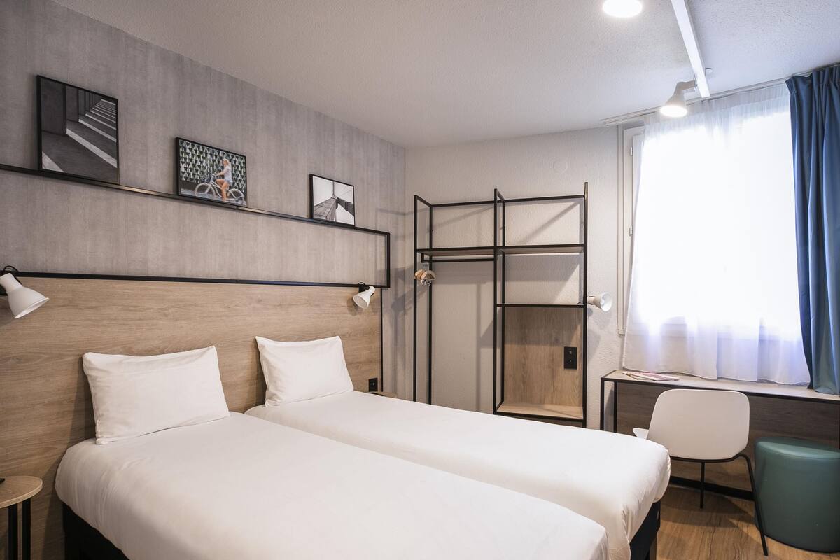 A hotel room with two beds, a desk, a chair, and a wardrobe.
