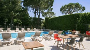 A poolside area with lounge chairs, tables, and a swimming pool. - ibis Avignon Sud (Avignon)