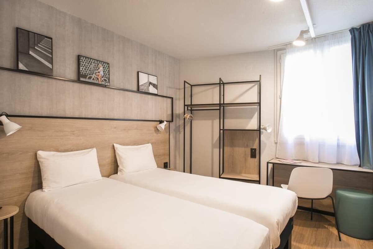 A hotel room with two beds, a desk, a chair, and a window with curtains.