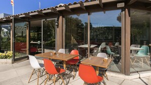 An outdoor patio with tables and chairs, large glass windows, and a clear blue sky. - ibis Avignon Sud (Avignon)