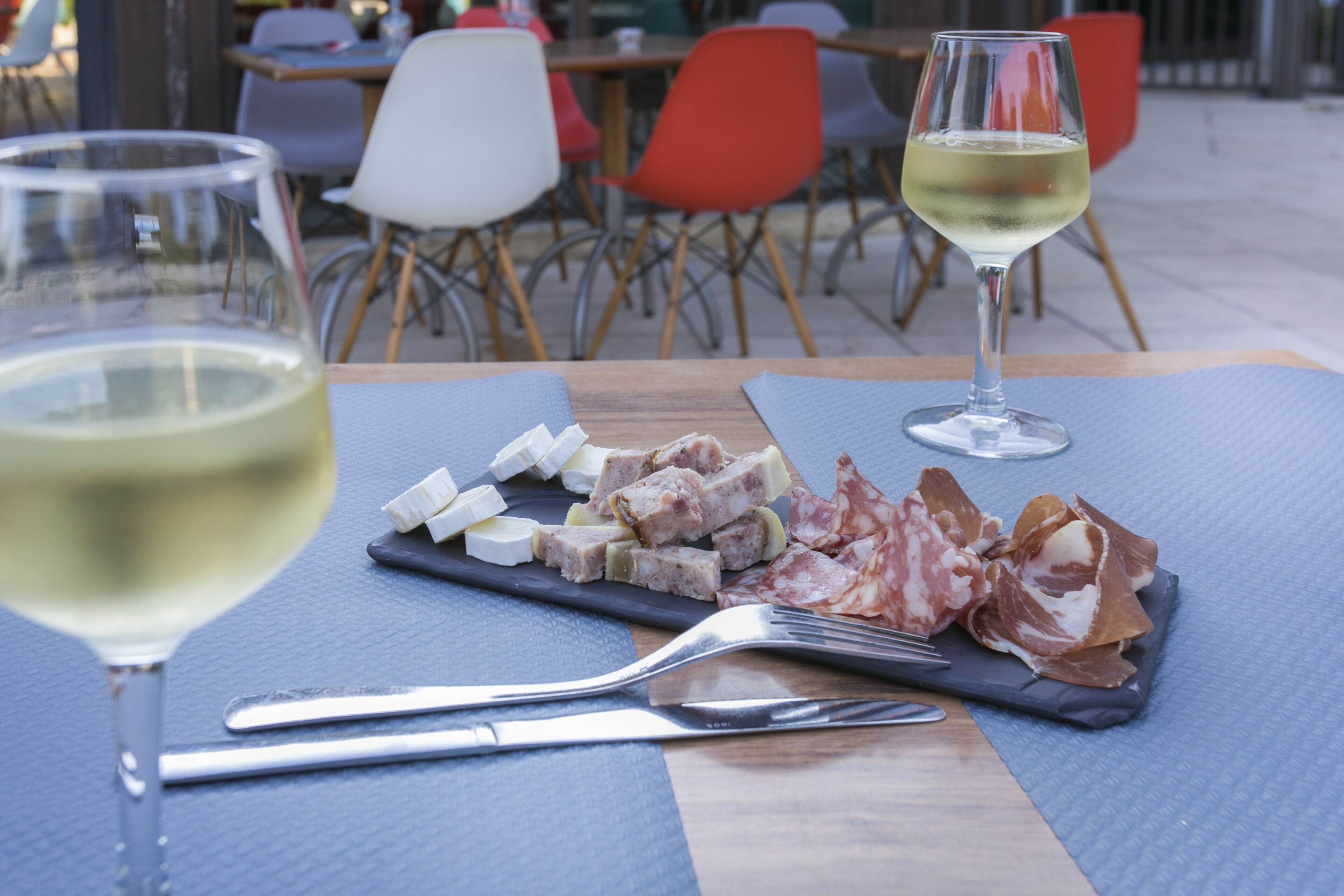 A table with a cheese and cured meat platter, a glass of white wine, and cutlery.