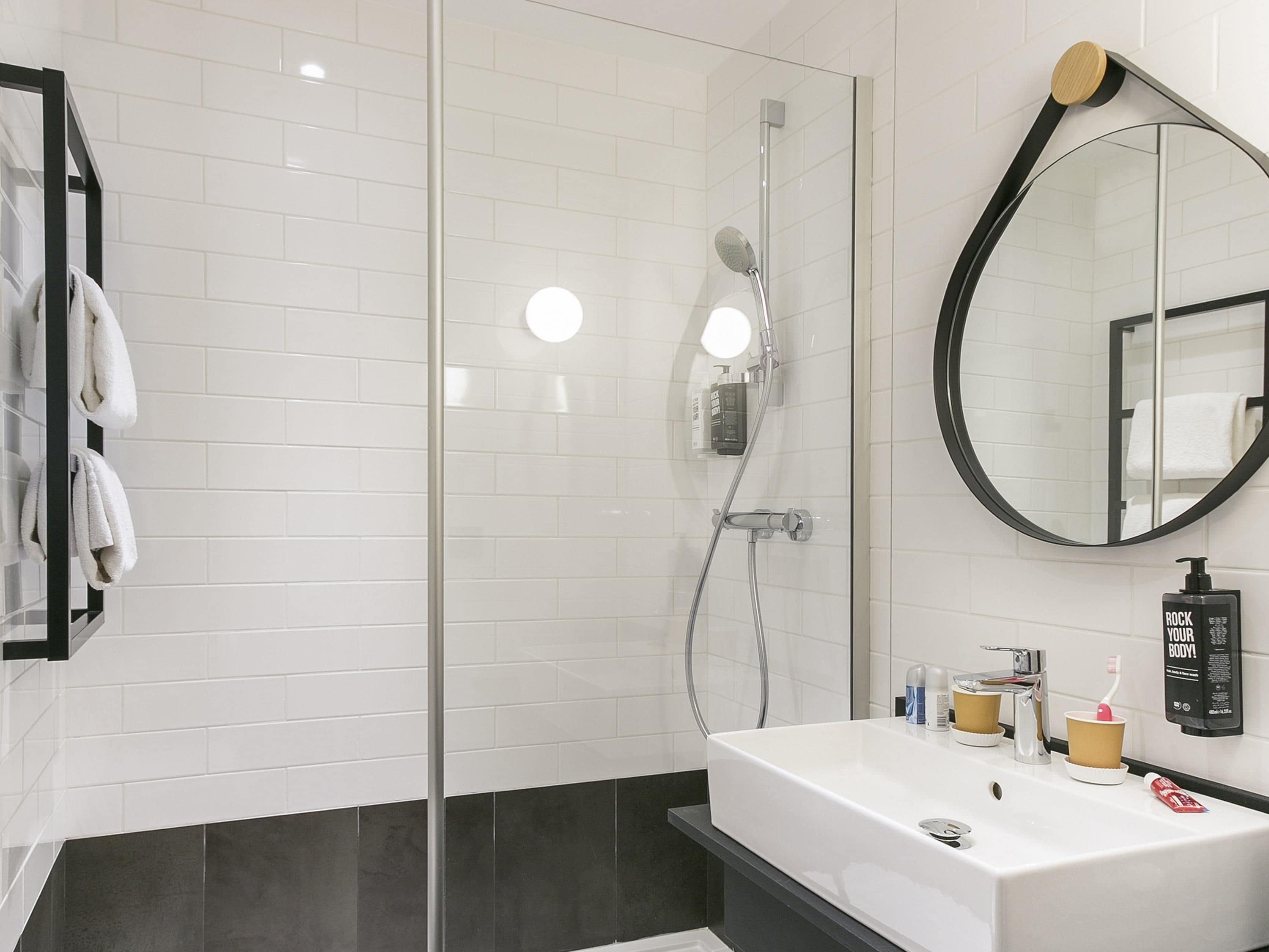 Un baño moderno con cabina de ducha de vidrio, un lavamanos blanco sobre encimera negra y un espejo grande.